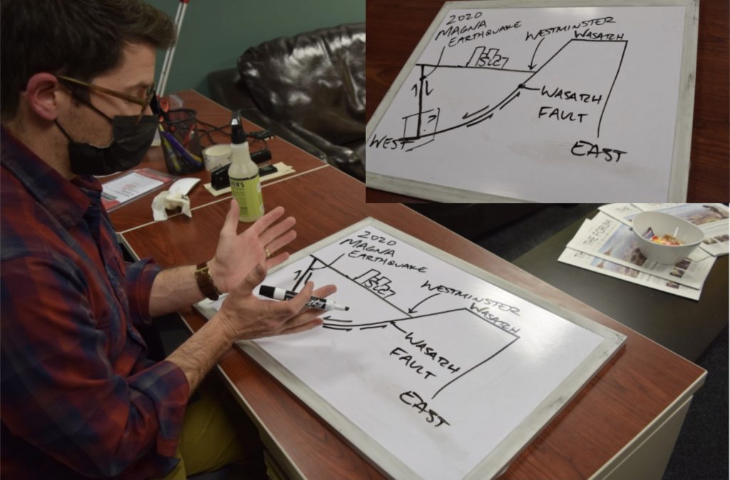 A man sitting at a desk illustrates the intersection of two fault lines under a city using a whiteboard.