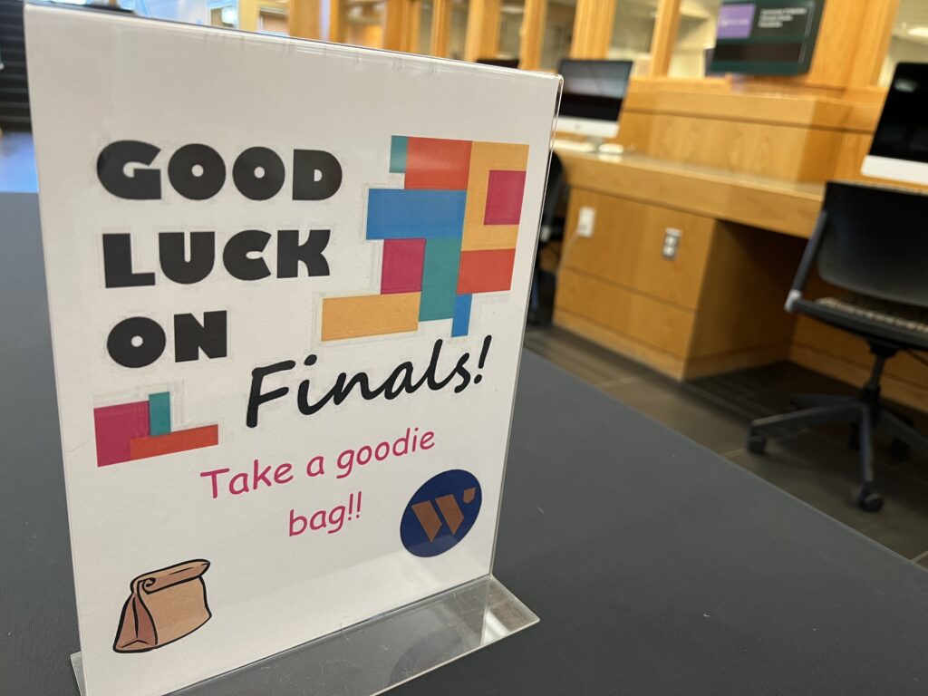 A sign that reads, “Good luck on finals! Take a goodie bag,” is displayed on an empty table with a black tablecloth. 