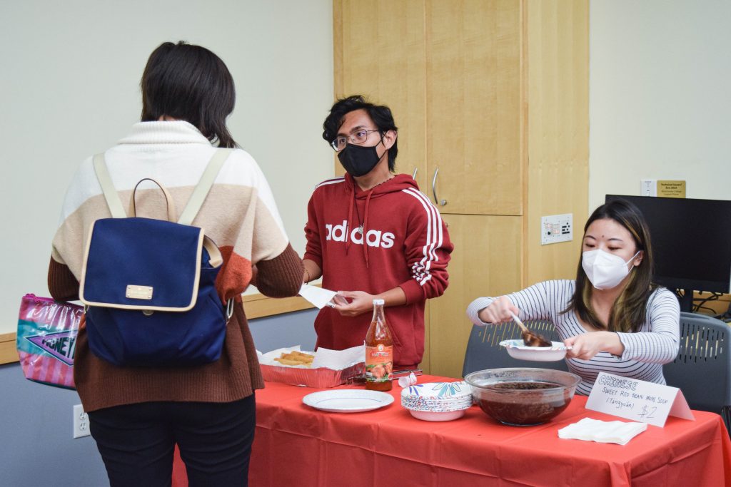 two students pass out food at a red table. 