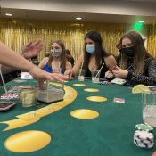 Three Westminster students in black tie attire sit at a Blackjack table at ASW Casino Night as the dealer reaches for cards.