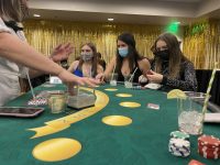 Three Westminster students in black tie attire sit at a Blackjack table at ASW Casino Night as the dealer reaches for cards.