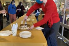 A woman in a red sweater serves chocolate pie at a long banquet table at the Annual Staff Council Pie Auction in Bassis Student Center as patrons gather around.