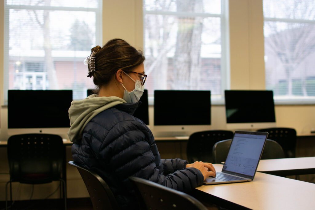 Former Griffin’s women’s soccer player Brynnae Braun, a woman with dark brown hair and glasses, types on a laptop in a Westminster College classroom.