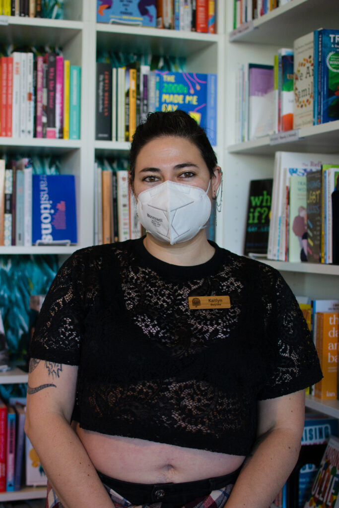Kaitlyn Mahone, the owner of Under the Umbrella, a queer bookstore, stands in front of their favorite section in the store, the nonfiction section on Feb. 26. 