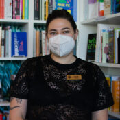 Kaitlyn Mahone, the owner of Under the Umbrella, a queer bookstore, stands in front of their favorite section in the store, the nonfiction section on Feb. 26.