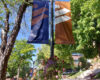 Two Westminster College banners, copper and dark purple, and a flower basket hang from a light post in Richer Commons.