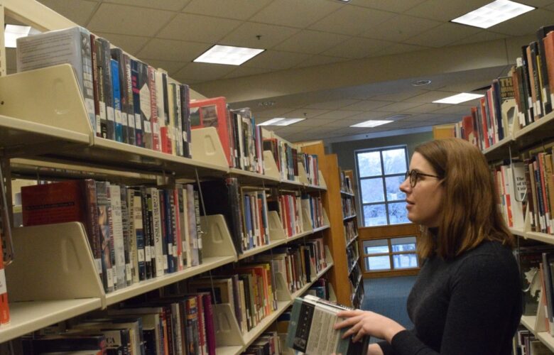 A woman stands and stacks books in a hallway of shelved books